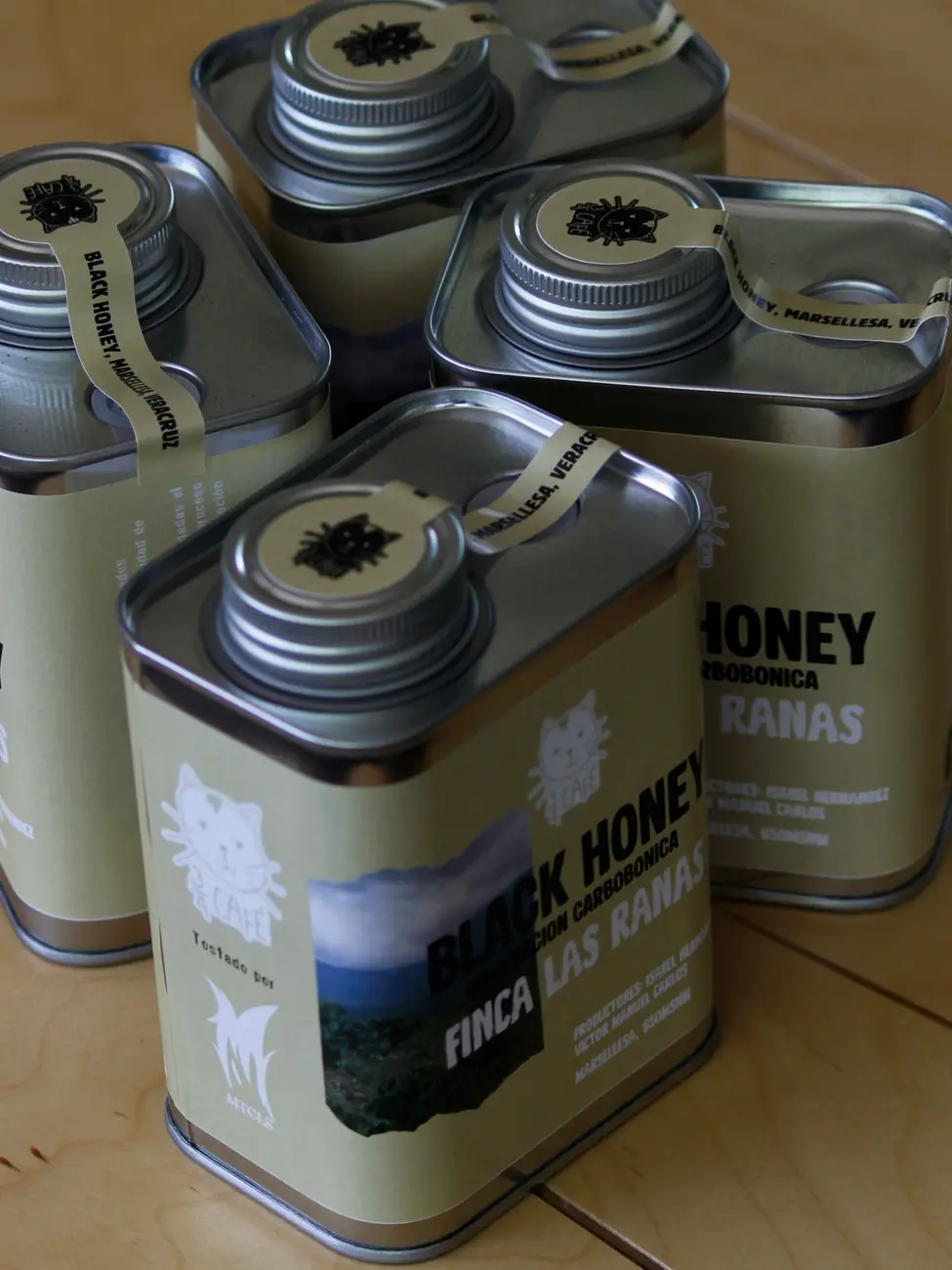 Latas de café de Tres Cuartos: Black Honey de Finca Las Ranas, sobre una mesa de madera